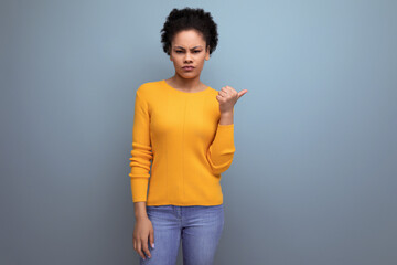 smart young latin woman with afro hair pointing finger to the side on gray background with copy space