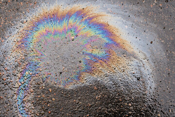 Close-up of an iridescent oil or gasoline spill on a wet asphalt, viewed from above. Bold...
