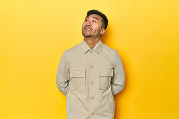 Obraz premium Asian man in stylish gray shirt on yellow studio relaxed and happy laughing, neck stretched showing teeth.
