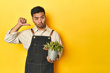 Asian gardener man holding a plant, yellow studio backdrop feels proud and self confident, example...