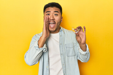 Asian man with invisible dental corrector, yellow studio backdrop shouting and holding palm near...