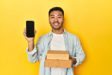 Asian man holding a food delivery and showing his phone on a yellow background