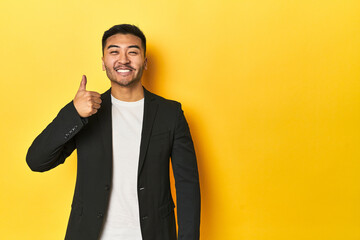 Asian man in black business jacket on yellow studio smiling and raising thumb up