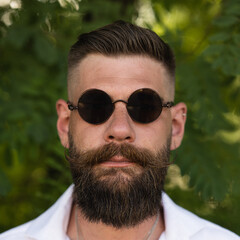 Set portrait. Man smoking a cigar by the river with long beard, shirt and curled moustache.
Dark...