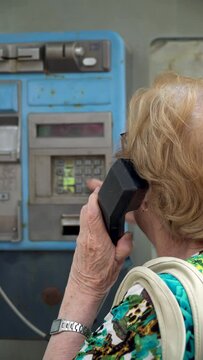 Senior woman dialing the phone number in an old phone booth