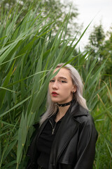 Fototapeta premium A young blonde girl in a black leather coat walks in the park and listens to music