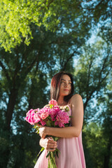Portrait of a young woman in a pink dress with flowers in nature