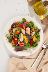 Salad with chicken, mango, strawberries and green leaves on a white background