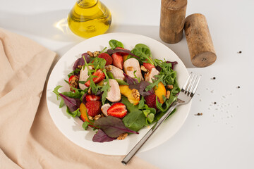 Salad with chicken, mango, strawberries and green leaves on a white background