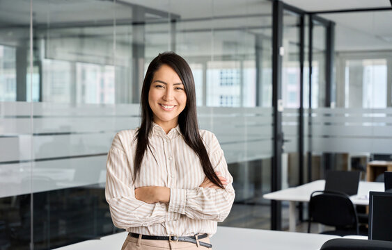 Confident smiling young professional Asian business woman corporate leader, happy japanese female employee, company sales marketing manager, standing arms crossed in office, portrait.