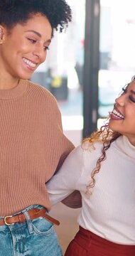 Two multi-ethnic women colleagues hug in the office, smiling and happy