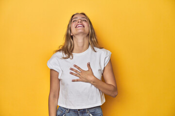 Young blonde Caucasian woman in a white t-shirt on a yellow studio background, laughs out loudly...