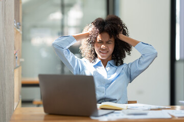 Young American businesswoman working on the laptop with documents and stressing at work from working on financial documents in office Overworked woman concept.