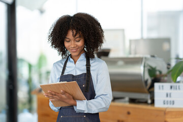 Beautiful african american female cashier or barista writing purchase details and checking...