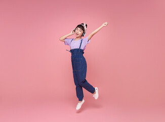 Fototapeta na wymiar Full length happy asian teen children girl wearing headphones listening to music and jumping on pink studio background. People lifestyle relax
