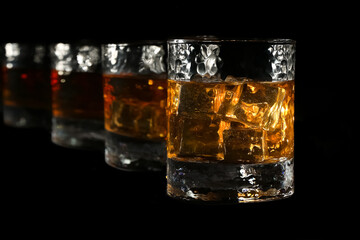 Four glasses of bourbon whiskey are illuminated by fire, and stand in one line towards the frame, on a black background