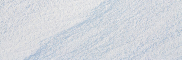 Beautiful winter background with snowy ground. Natural snow texture. Wind sculpted patterns on snow surface. Wide panoramic texture for background and design.