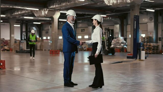 Positive Mature Man Shaking Hands with Young Beautiful Lady Warehouse Employee and Talking. Handshake of Professional Workers in Repository. Cooperation Concept