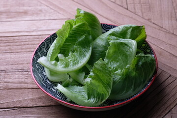 Romaine or cos lettuce is a variety of lettuce that grows tall heads of sturdy dark green leaves with firm ribs down the center. Romaine lettuce in a ceramic dish. Lactuca sativa. Selada romaine.