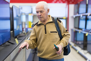 elderly grayhaired man pensioner looking counter with modern digital televisors in showroom of digital goods store