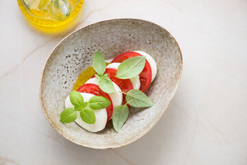 Beige bowl with italian traditional caprese salad, horizontal shot on a beige marble background, top view