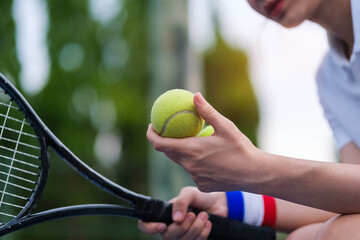 Closeup of female hand holding tennis ball and racket while playing tennis on a sunny day.