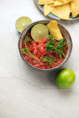 Bowl of tomato salsa with nachos on a beige stone background, vertical shot with space, elevated view
