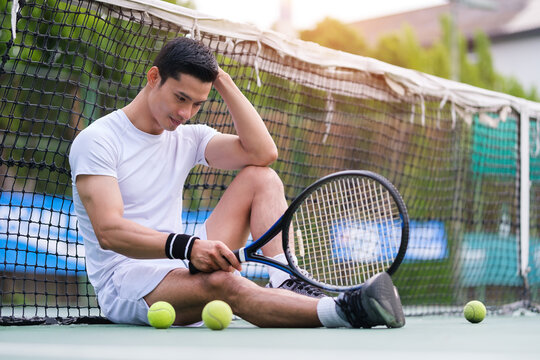 Exhausted man tennis player sitting on the court looking disappointed after practice.