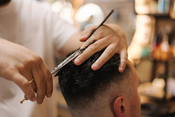 Hairdresser cutting hair using scissors and comb. Professional barber serves the client