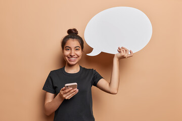 Cheerful Latin woman wearing casual black t shirt holds modern smartphone and white communication...