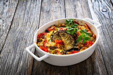 Bread casserole with mozzarella cheese, scrambled eggs, aubergine and tomatoes on wooden table
