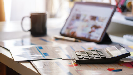 Accounting work space with digital tablet, calculator, financial graph and tables on wooden desk. © wattana