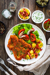 Breaded fried pork chop with fresh vegetable salad and potatoes on wooden table
