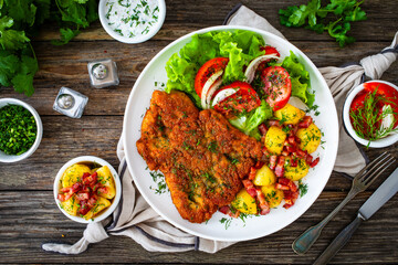 Breaded fried pork chop with fresh vegetable salad and potatoes on wooden table
