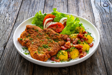 Breaded fried pork chop with fresh vegetable salad and potatoes on wooden table

