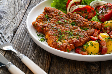 Breaded fried pork chop with fresh vegetable salad and potatoes on wooden table
