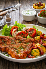 Breaded fried pork chop with fresh vegetable salad and potatoes on wooden table
