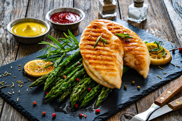 Grilled chicken breasts and green asparagus on wooden table

