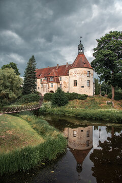 View to old mediewal Jaunpils castle reflected in a pond on overcast summer day in Latvia.