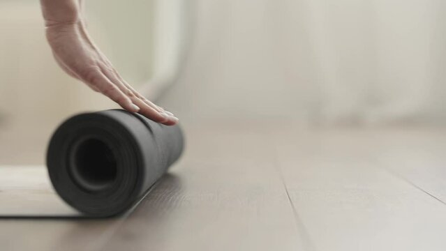 Close up shot of young adult Caucasian female unrolling yoga mat before yoga practice at home.