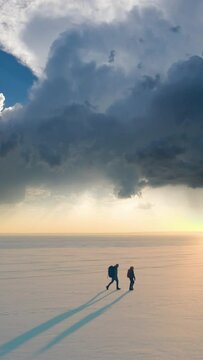 The two people with backpacks trekking through the icy snow field