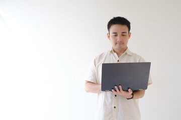 A young Asian man wearing a beige shirt and a smartwatch on his left wrist is using a black laptop withstanding. Isolated white background. Suitable for advertisement.