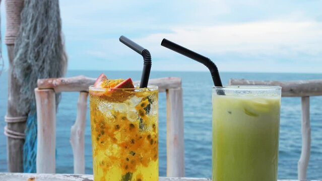 Two glasses with soft drinks with straws on the table. Non-alcoholic tropical drink with passion fruit and milk matcha latte. The black straws in exotic vegan drinks flutter in the wind. Ocean breeze.