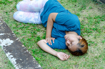 Asian woman lying on her side fainting on grass in the park in summer because of the hot weather