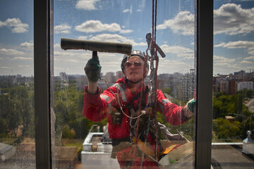 A blurry view through a dirty window of a window washer. Rope access. An alpinist washes windows