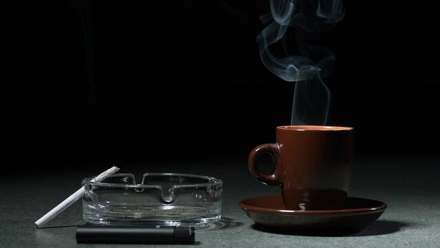 Cup with hot coffee and a cigarette in an ashtray on the table. Slow motion