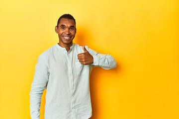 African American man in blue shirt, yellow studio, smiling and raising thumb up