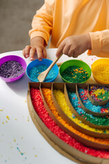 Child hands playing colored rice and make rainbow. Child filled the rainbow with bright rice. Montessori material. Sensory play and learning colors activity for kids.