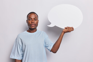 Horizontal shot of serious African man dressed in casual t shirt holds communication bubble with empty space for your promotional content isolated over white background. Place your text here