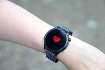 Smart watch on female hand measuring heart rate. Round display with app for health monitoring